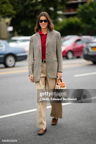 Guest wears black sunglasses, a red polo shirt, a gray and black checkered print pattern blazer jacket, a black shiny leather belt, beige large...