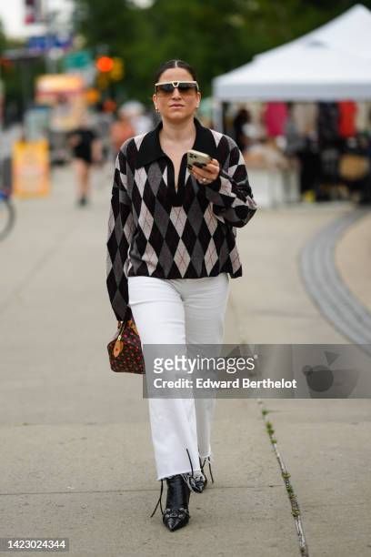 Guest wears beige and brown futurist sunglasses, silver rings, a black / gray / white checkered jacquard print pattern wool polo oversized shirt,...