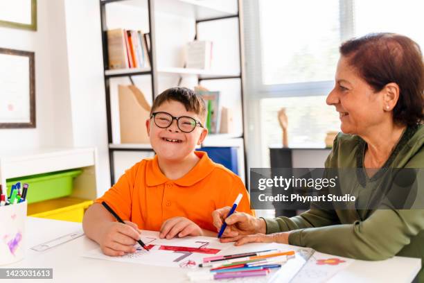 ein junge mit down-syndrom ist mit seinem lehrer in einem klassenzimmer - developmental disability stock-fotos und bilder