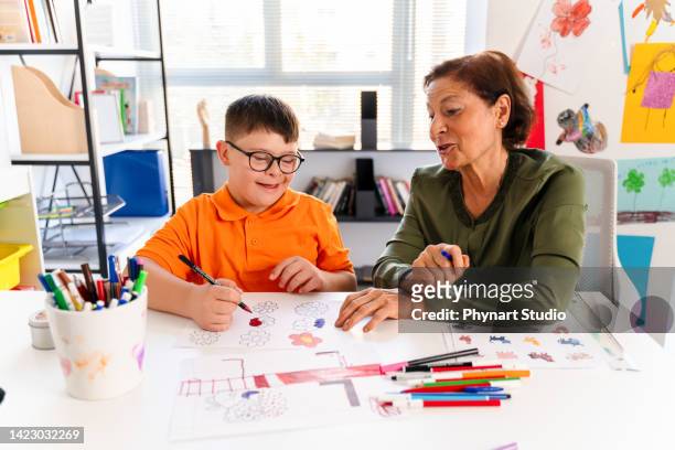 a boy with down syndrome is in a classroom with his teacher - elderly cognitive stimulation therapy stockfoto's en -beelden