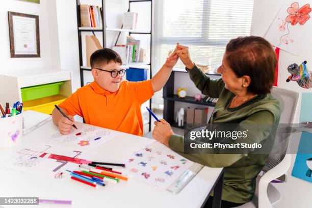 a boy with down syndrome is high five in a classroom with his teacher - learning disability care stock pictures, royalty-free photos & images