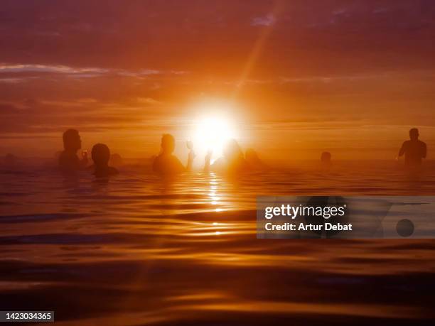 people relaxing in thermal pool with an infinity view with silhouette against the sun in iceland. - lagoon stock pictures, royalty-free photos & images