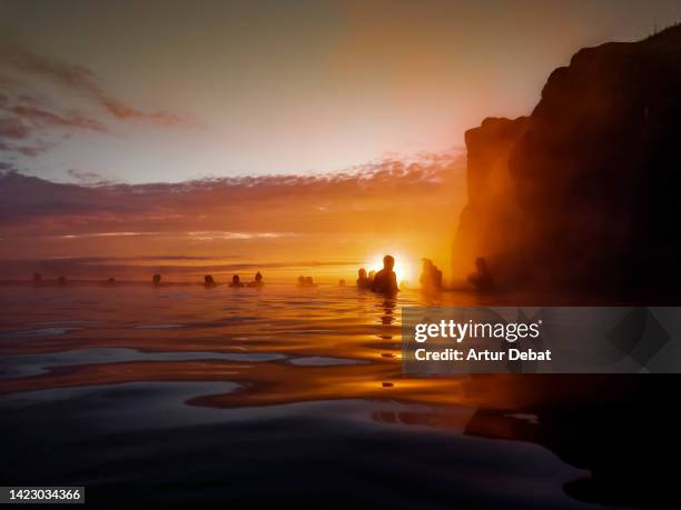people relaxing in thermal pool with an infinity view with silhouette against the sun in iceland. - lagon photos et images de collection