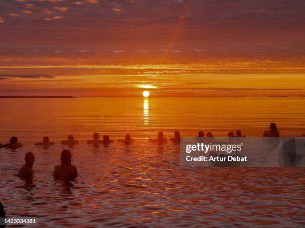 people contemplating the sunset from thermal pool with infinity view in iceland. - lagune stockfoto's en -beelden