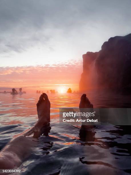 man relaxing floating on water with feet against the sunset in a hot spring infinity pool in iceland. - lagune stockfoto's en -beelden