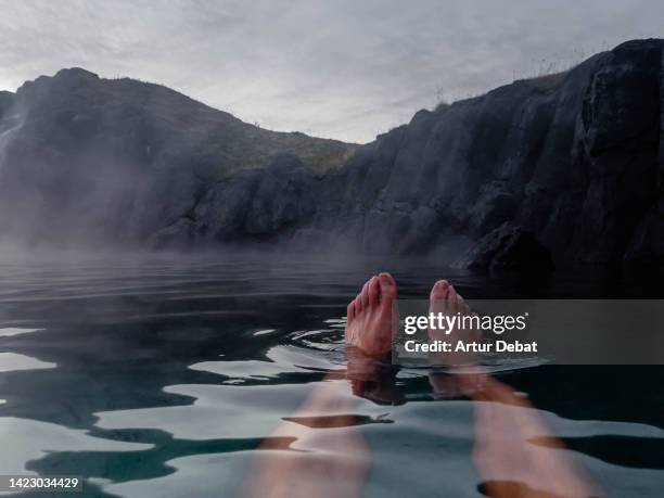 man relaxing floating on water with feet in a hot spring in iceland. - foot spa stock pictures, royalty-free photos & images