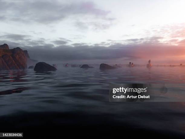 people contemplating the sunset from thermal pool with infinity view in iceland. - lagoon stock pictures, royalty-free photos & images