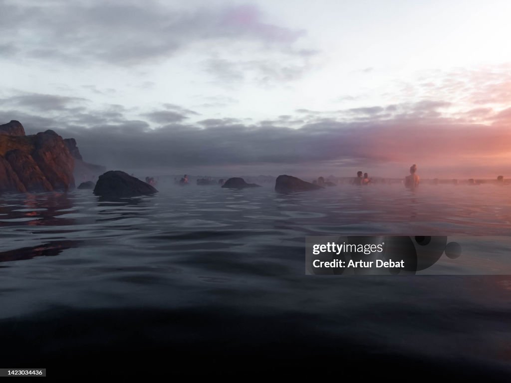 People contemplating the sunset from thermal pool with infinity view in Iceland.