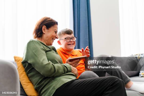 niño pequeño con síndrome de down disfruta pasar tiempo con la madre y ver el teléfono móvil - down's syndrome fotografías e imágenes de stock