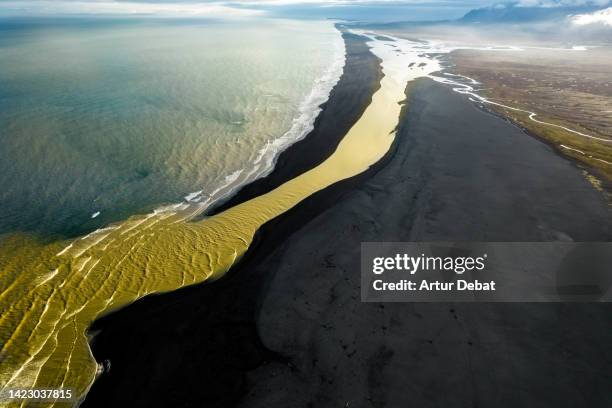 glacier river with yellow color fall into the ocean coast in iceland. - sediment stock-fotos und bilder