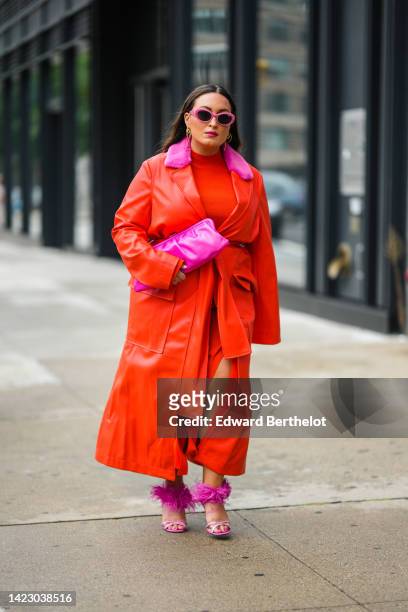 Guest wears pink sunglasses, gold earrings, a neon red turtleneck long slit dress, a red shiny leather long trench coat with embroidered neon pink...