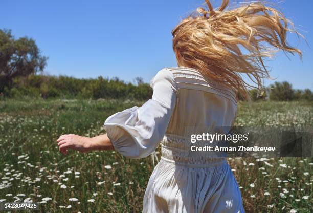 happy blond woman running among the grass and flowers in the meadow. nicely fits for a book cover - woman fresh air photos et images de collection