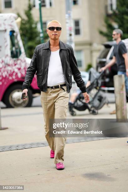 Guest wears black sunglasses, a white t-shirt, a black shiny leather bomber coat, a black shiny leather belt, beige suit pants, neon pink suede...