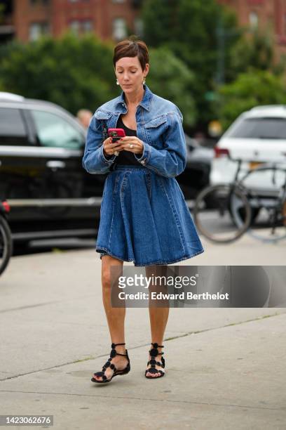 Guest wears gold and crystal pendant earrings, a blue denim cropped jacket, a matching blue denim plated knees skirt, a black tank-top, black suede...