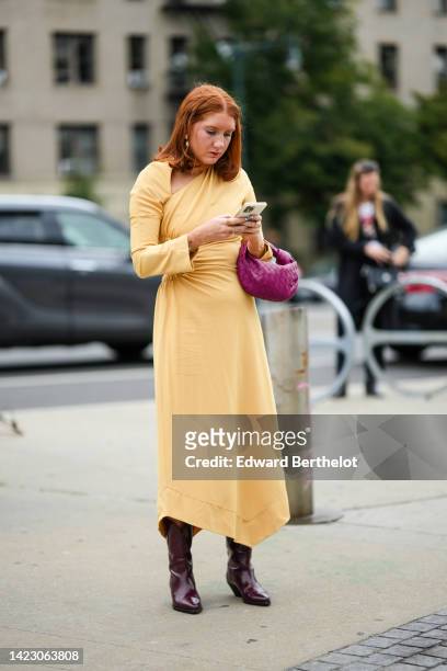 Guest wears gold earrings, a pale yellow asymmetric / cut-out shoulder / long sleeves long dress, a purple pink shiny leather braided Jodie handbag...