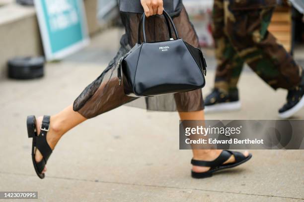 Guest wears a black shiny varnished leather handbag from Prada, black tulle long skirt, black shiny leather strappy sandals , outside Ulla Johnson,...