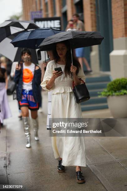 Guest wears a white latte puffy long sleeves ruffled blouse, a matching long white latte long skirt, a black shiny leather handbag, black shiny...