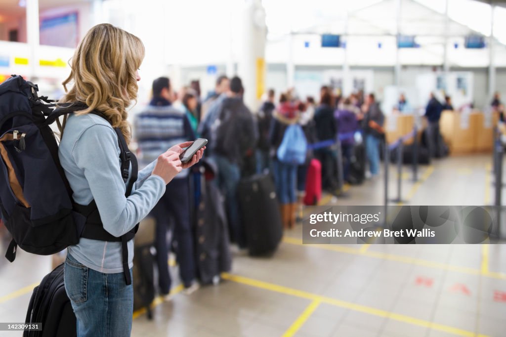 Female traveller texting at airport check-in desk