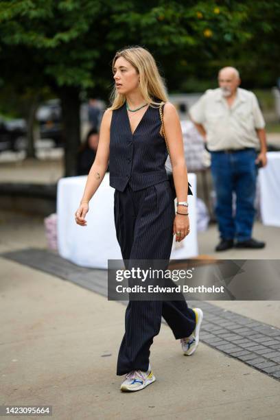 Guest wears a green pearls necklace, a black striped print pattern buttoned / sleeveless gilet, matching black striped print pattern suit pants, a...