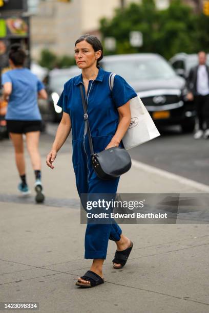 Guest wears a white shopping shoulder bag, a black shiny leather shoulder bag, a navy blue denim short sleeves / zipper jumpsuit, black sandals ,...