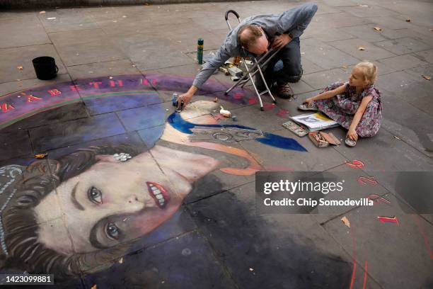 Three-year-old Violet Williams watches as chalk artist Julian Beever works on a portrait of Queen Elizabeth II on the sidewalk near Trafalgar Square...