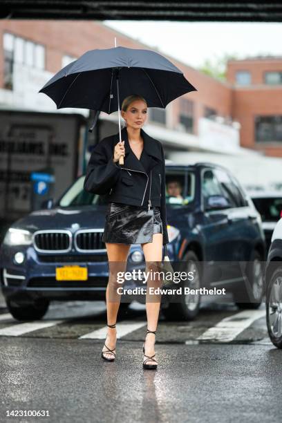 Leonie Hanne wears a black umbrella, a silver and black Triangle pendant earrings from Prada, a black felt / zipper / oversized cropped jacket, a...
