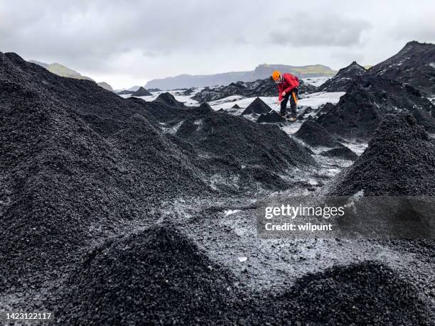 young male standing between lava ash ice pyramids on a glacier hitting away with ice axe - icepick stock pictures, royalty-free photos & images