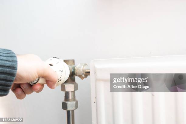 view of person adjusting the temperature of a radiator. energy prices has increased a lot. - energieeffizienz stock-fotos und bilder