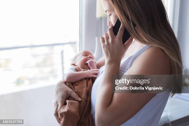 mother holding newborn baby when calling doctor's office via phone - new user stockfoto's en -beelden