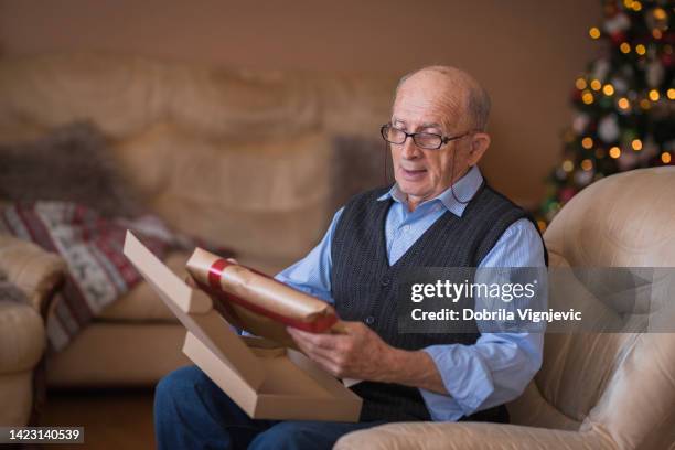 elderly man opening christmas present at home - elderly receiving paperwork stock pictures, royalty-free photos & images