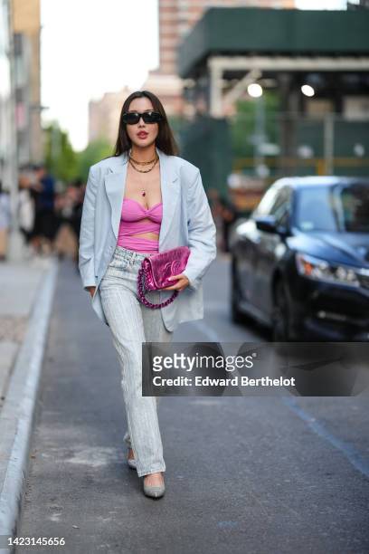 Guest wears black sunglasses, gold large chain necklace, a pink strappy / cut-out body, a pale blue oversized blazer jacket, a pink metallic shiny...