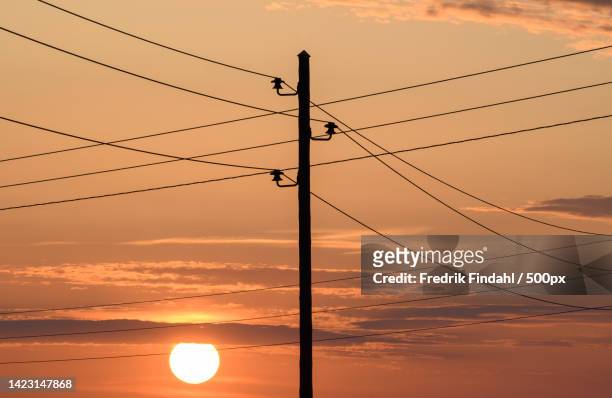 low angle view of silhouette of electricity pylon against orange sky - väder stock pictures, royalty-free photos & images