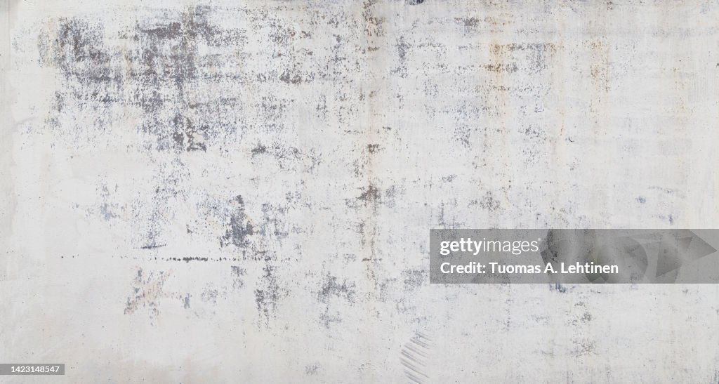Front view of a weathered, aged and dirty wall, white plastered and painted surface peeling off.