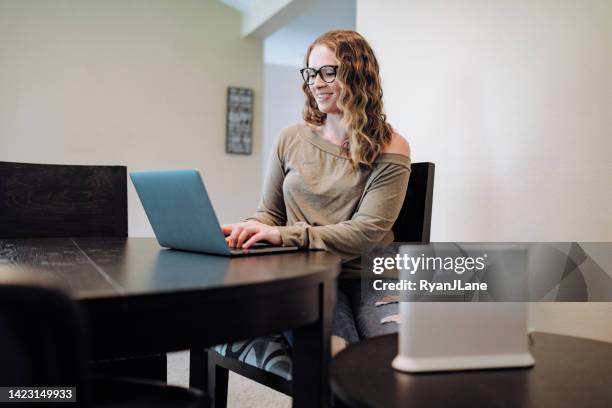 woman using laptop in apartment dining room - draadloze technologie stockfoto's en -beelden