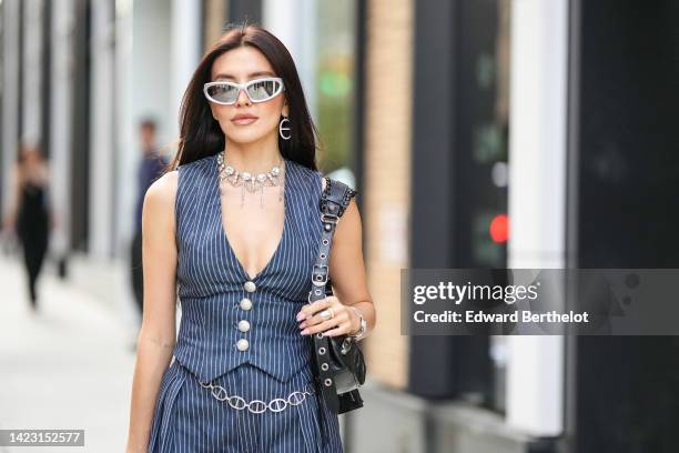 Guest wears silver sunglasses, silver earrings, a large silver chain necklaces, a navy blue striped print pattern V-neck / sleeveless / buttoned...