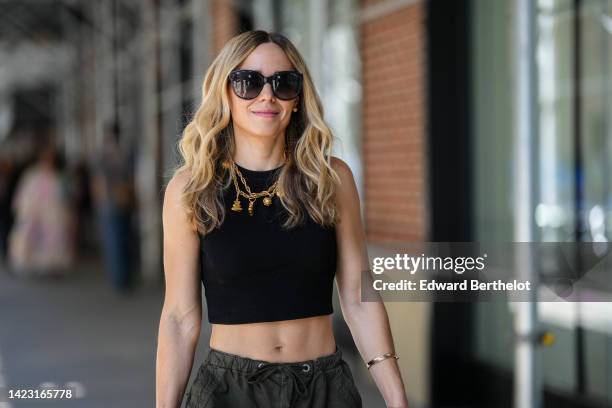 Guest wears black sunglasses, a gold large chain necklace, a black halter-neck cropped tank-top, gold bracelets, silver and diamonds rings, khaki...