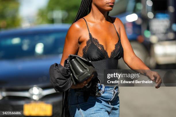 Guest wears a black lace print pattern v-neck tank-top, a black shiny leather grained handbag from Chanel, blue denim large shorts, outside...