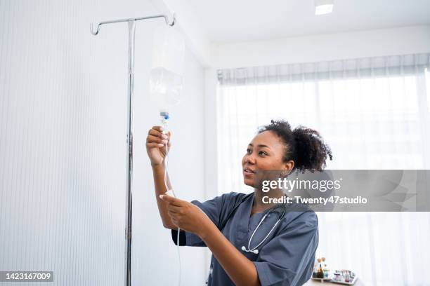 young black nurse preparing iv drip in hospital ward - iv drip womans hand fotografías e imágenes de stock