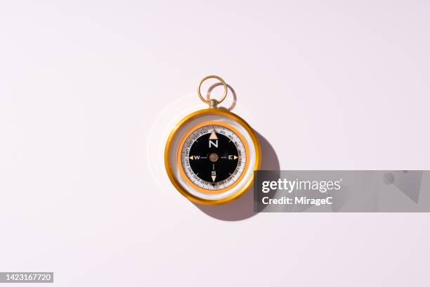 gold colored navigational compass on pink background - bussola foto e immagini stock