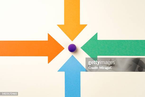 four arrows point to a purple sphere point in focus - aiming concept stock pictures, royalty-free photos & images