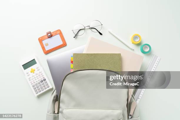 college school supplies out of a backpack on green - papier tasche offen stock-fotos und bilder
