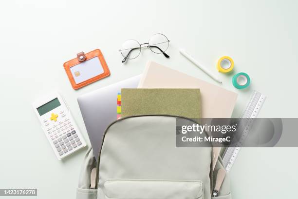 college school supplies out of a backpack on green - utiles escolares fotografías e imágenes de stock