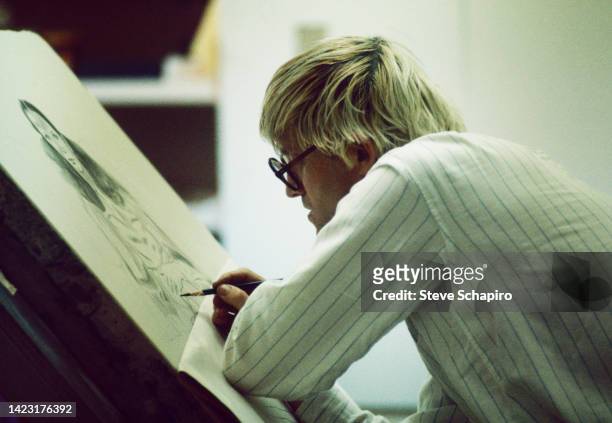 Profile view of English artist David Hockney as he paints at an easel, Los Angeles, California, 1965.