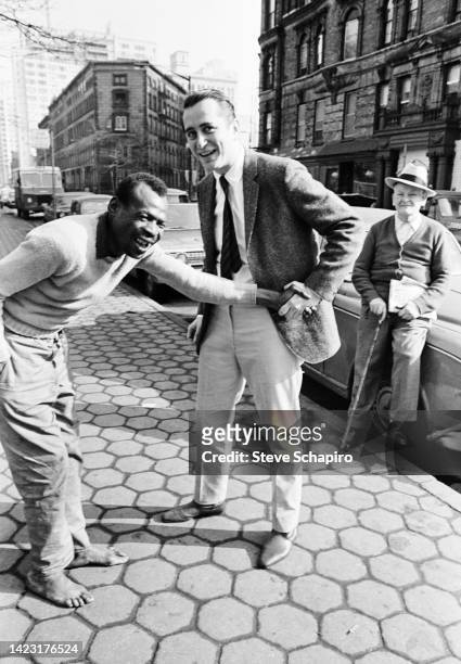 An unidentified, shoeless man shakes hands with American film director and actor Robert Downey Sr on an unspecified street, New York, New York, 1967.