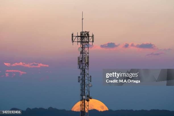 full moon rising from the horizon behind a communications tower. - hora azul crepúsculo fotografías e imágenes de stock