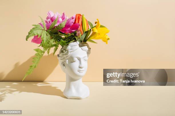 retro head sculpture with flowers on beige background. creative positive thinking concept. minimal mental health awareness month. psychology, emotional wellness, progress, flowering, work on yourself idea - geestelijke gezondheid stockfoto's en -beelden