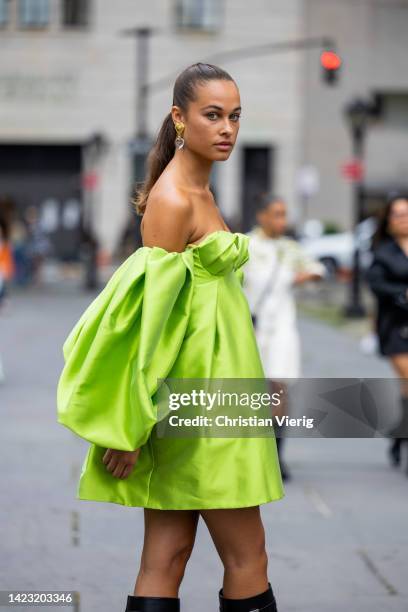 Sarah Lysander wearing green off shoulder dress, black knee high boots, white bag outside Carolina Herrera on September 12, 2022 in New York City.