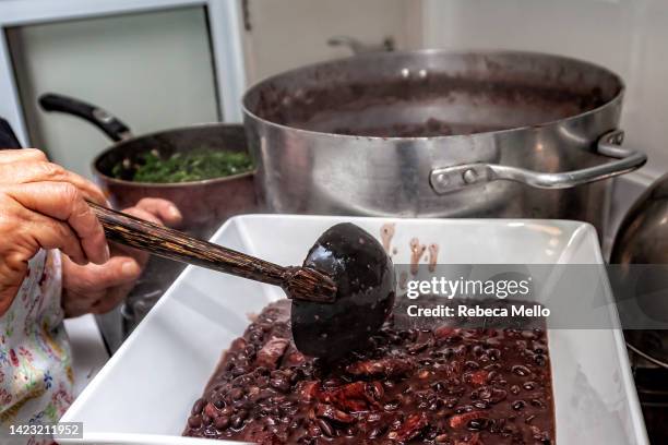 serving the beans and pork, brazilian  feijoada,  in a white bowl. - brazilian feijoada dish stock pictures, royalty-free photos & images