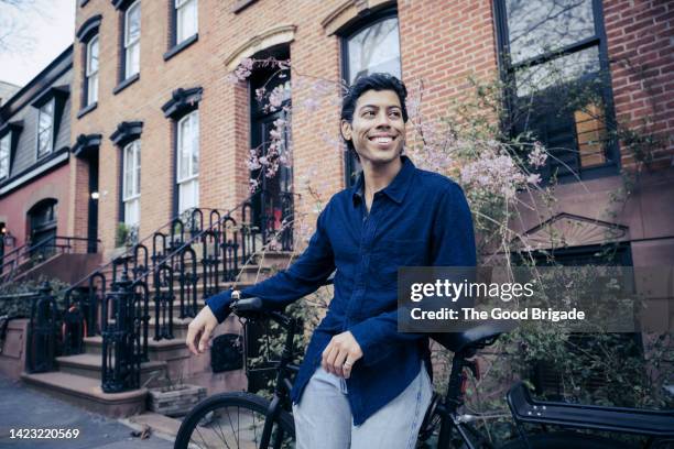 happy man leaning on bicycle on city sidewalk - brooklyn brownstone foto e immagini stock