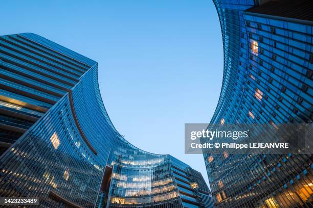 modern curved glass skyscraper facades reflecting clear blue sky at night - china town stock-fotos und bilder